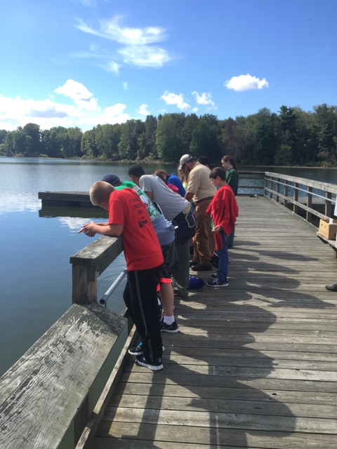 middle school students observing water sampling equipment at lake